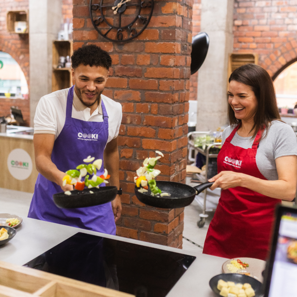 A man and a woman tossing vegetable in a frying pan and enjoying a cookery class.